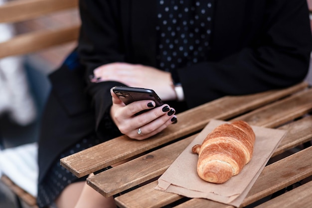 Cute girl having breakfast on the terrace while using on her\
smart phone student makes a study plan sitting in an outdoor cafe\
during breakfast