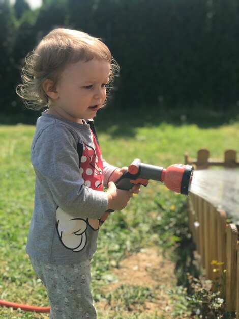 Photo cute girl holding garden hose in yard