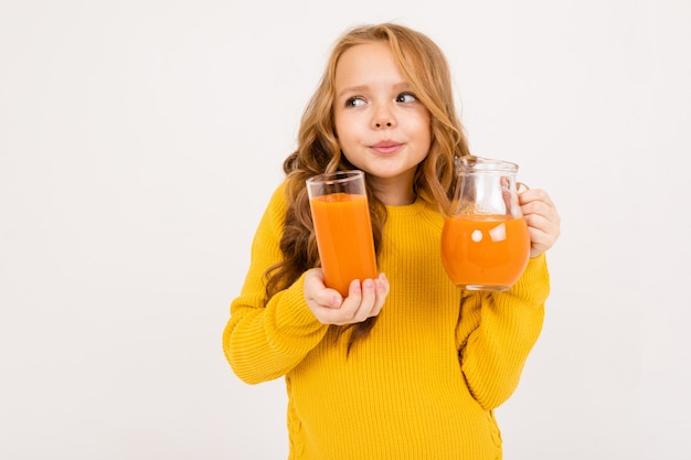 Cute girl holding a glass and a jug with carrot juice on an isolated white background