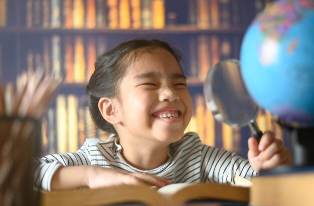 cute girl holding magnifying glass while studying on table