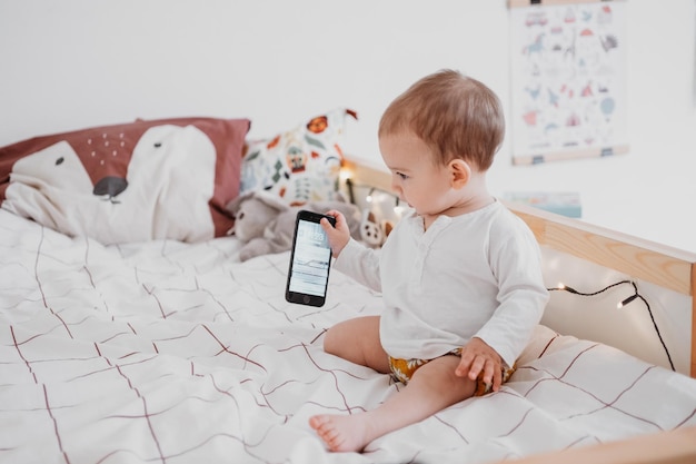 Photo cute girl holding mobile phone sitting on bed at home