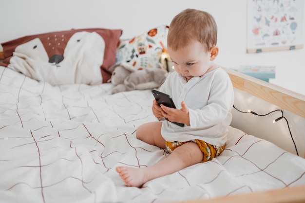 Photo cute girl holding mobile phone sitting on bed