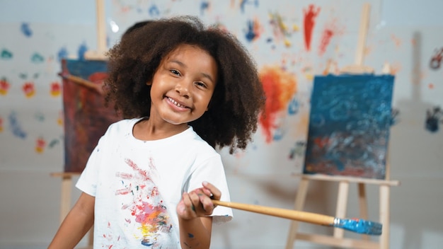 Photo cute girl holding painted brush while student drawing canvas behind erudition