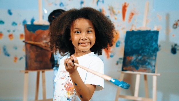 Cute girl holding painted brush while student drawing canvas behind Erudition