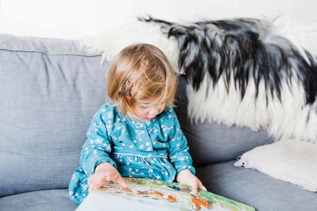 cute girl holding picture book sitting on sofa at home