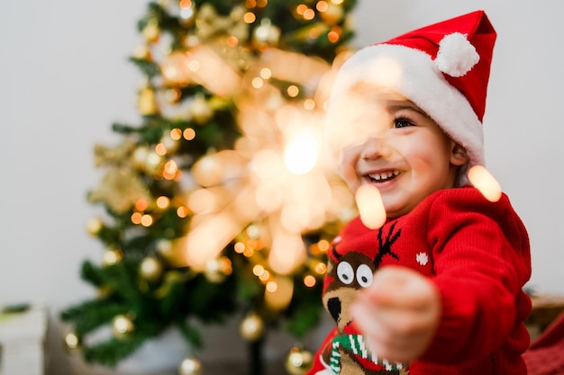 クリスマスツリーに座ってスパークラーを握っている可愛い女の子