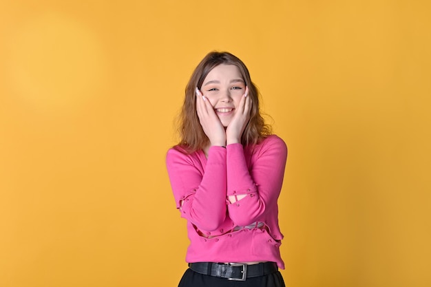 A cute girl holds her face in her hands and laughs on a bright yellow background Human emotions