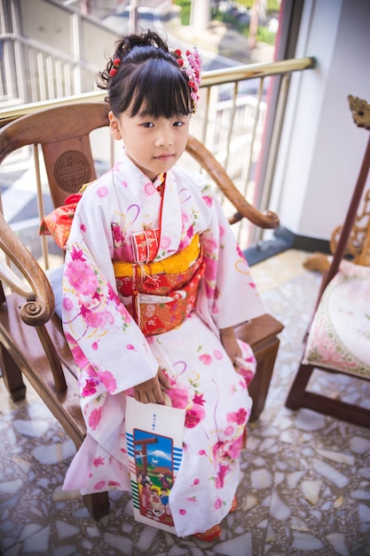 写真 キモノを着た可愛い女の子が自宅の椅子に座っている