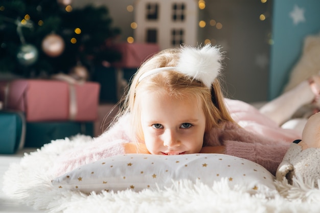 Cute girl is lying on her stomach on a pillow near a Christmas tree