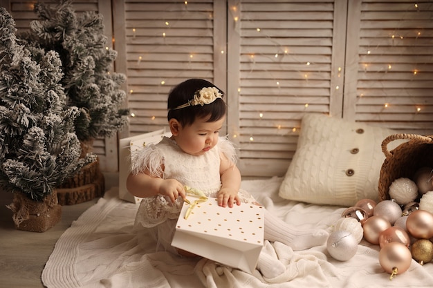 A cute girl is sitting on a knitted blanket and playing with a\
package of gifts for the new year