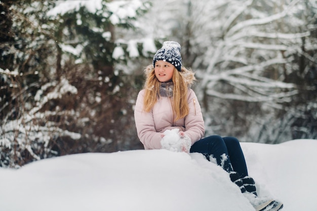 Милая девушка сидит на горе снега и делает снежки