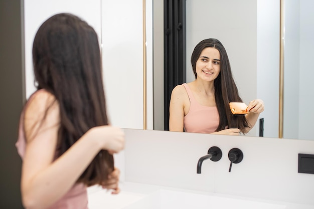 Cute girl is standing in the bathroom and combing her long hair