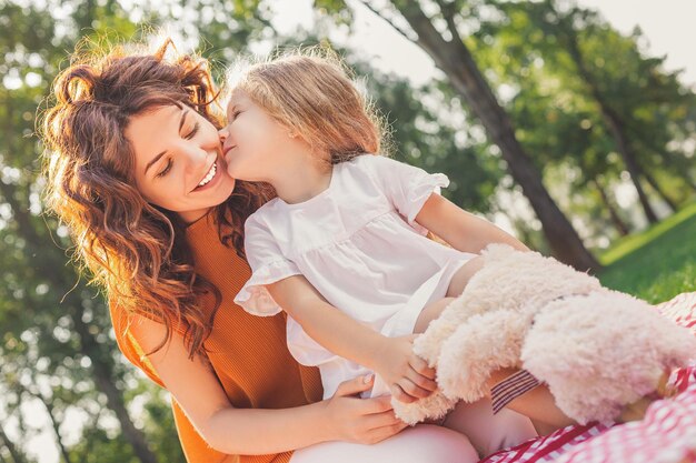 公園の毛布の上に座っている彼女の母親にキスするかわいい女の子