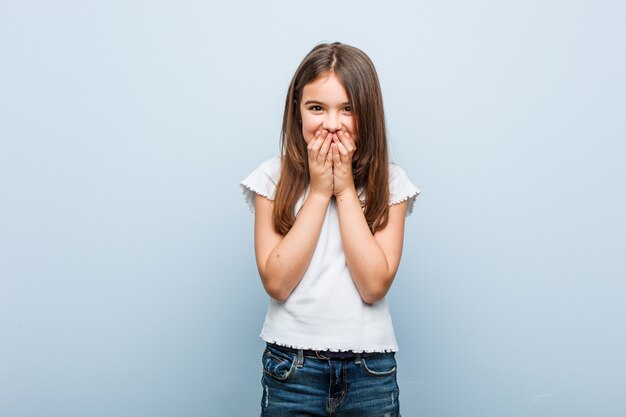 Cute girl laughing about something, covering mouth with hands.