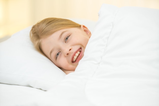 The cute girl lay on the bed with white linens