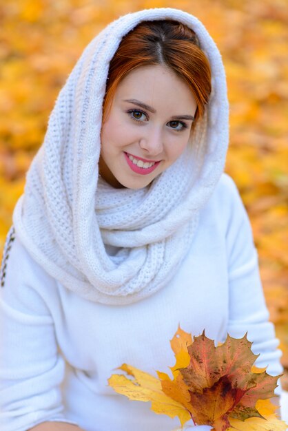 Cute girl in long white wedding dress posing in rural path among autumnal trees iin golden hour atmosphere.