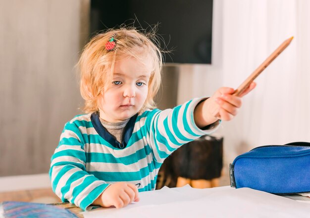 cute girl looking away while holding pencil at home
