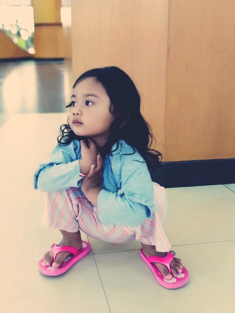 Cute girl looking away while sitting on floor at home