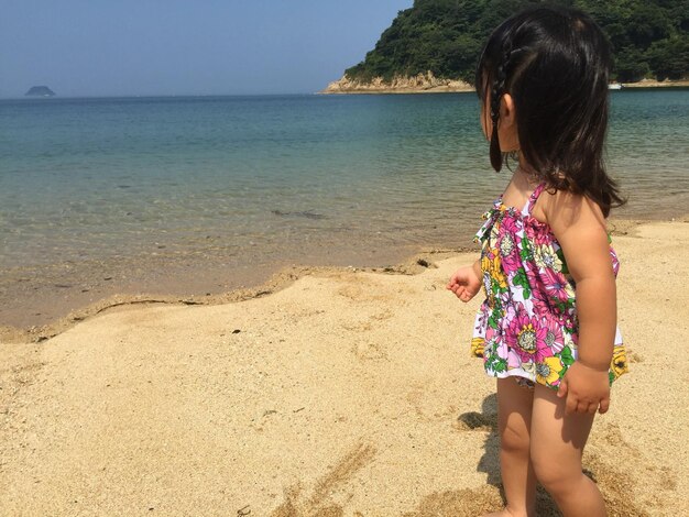 Photo cute girl looking away while standing on beach