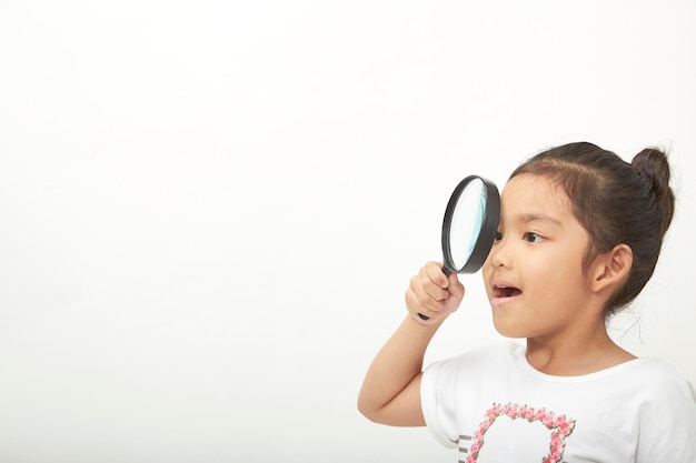 Photo cute girl looking through magnifying glass against white background