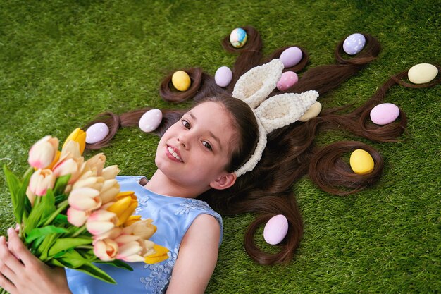 부활절 달걀으로 잔디에 누워 귀여운 여자. 부활절 달걀은 그녀의 머리카락에 있습니다.
