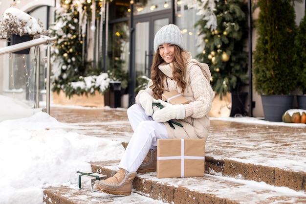 A cute girl in mittens sits on the steps and enjoys gifts on the street in winter in the city