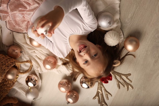 a cute girl in a New Years costume is lying on the floor Christmas balls are around the girl