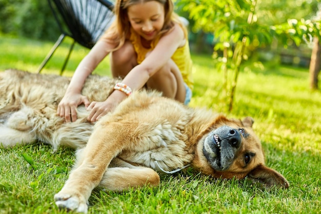 Cute girl and old dog enjoy summer day on the grass in the park