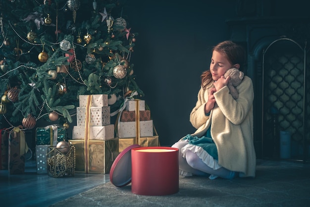 Cute girl opening present next to cristmas tree