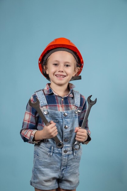 A cute girl in an orange hard hat posing on blue background, holding wrenches in both hands. Construction and repair concept.