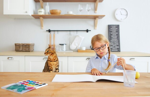 Cute girl painting on book with cat by table