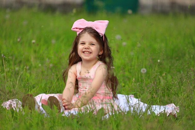 Cute girl in a pink dress with a hat sits on the grass in the park. High quality photo