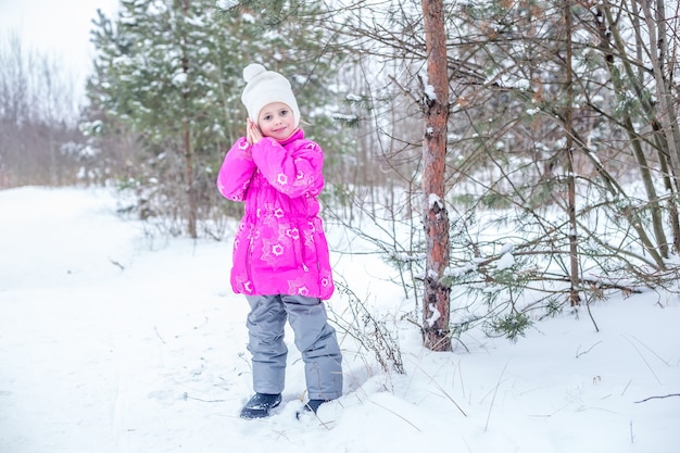 Cute girl in pink warm clothes playing in the winter forest, spending time outdoors in winter