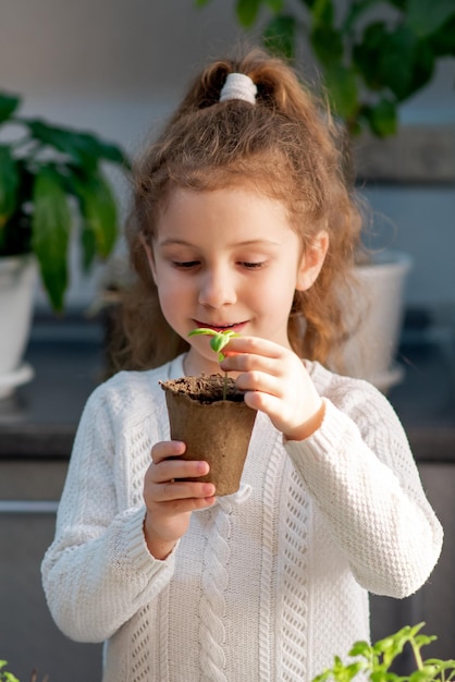 A cute girl plants at home in eco pots She is wearing a white sweater The garden of the house Hobby