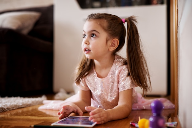 Cute girl playing games on her tablet. Wearing pigtails in her hair.