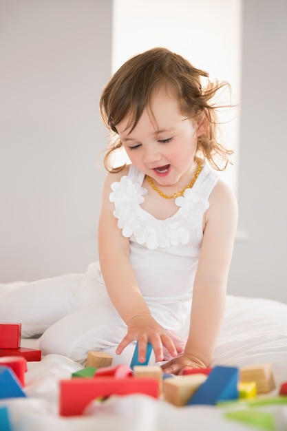 Cute girl playing with building blocks on bed