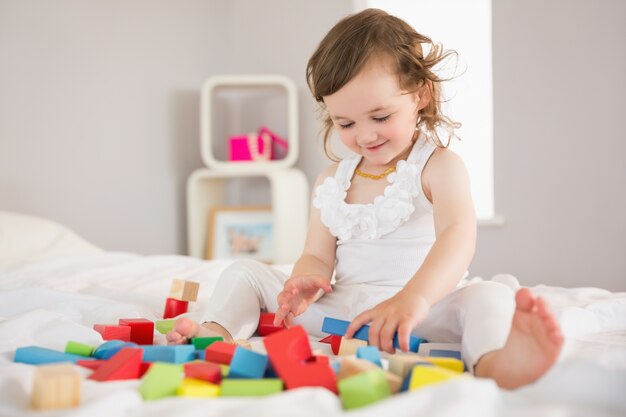 Cute girl playing with building blocks on bed