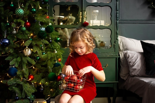 写真 屋内のクリスマス ツリーの近くのクリスマスの装飾で遊ぶかわいい女の子メリー クリスマスとハッピー ホリデー