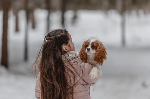 Ragazza carina che gioca con il cane nella foresta del parco invernale