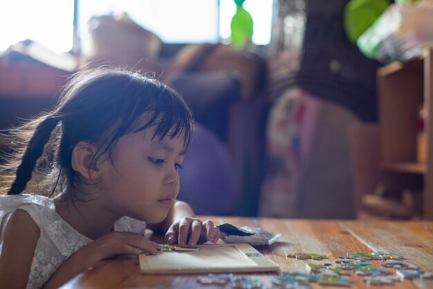 写真 可愛い女の子が自宅のテーブルの上でパズルで遊んでいます