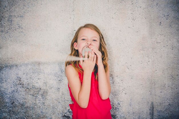 Photo cute girl playing with tin can phone while standing against wall