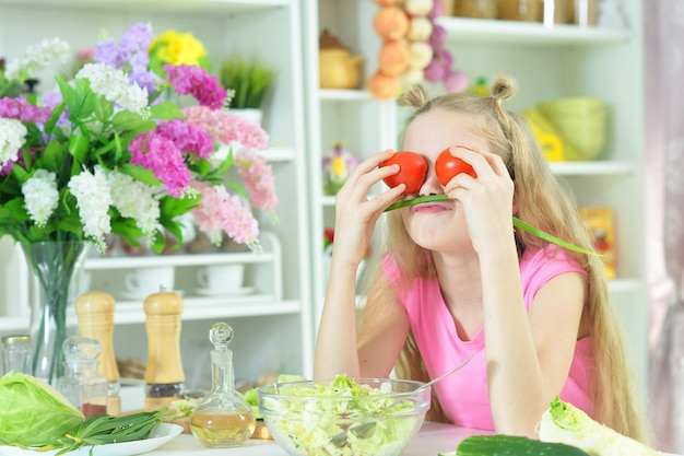 Cute girl playing with tomatoes in kitchen at home