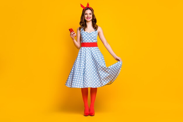 Cute girl in polkadot dress red tights hold cellphone on yellow background