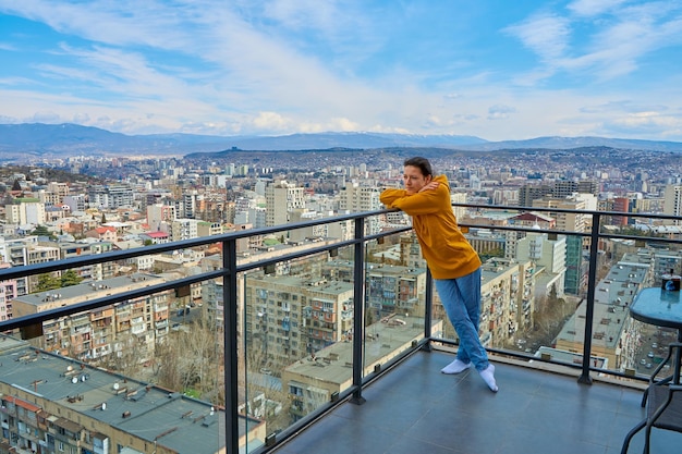 Симпатичная девушка позирует, стоя на балконе высокого этажа небоскреба с городским пейзажем позади