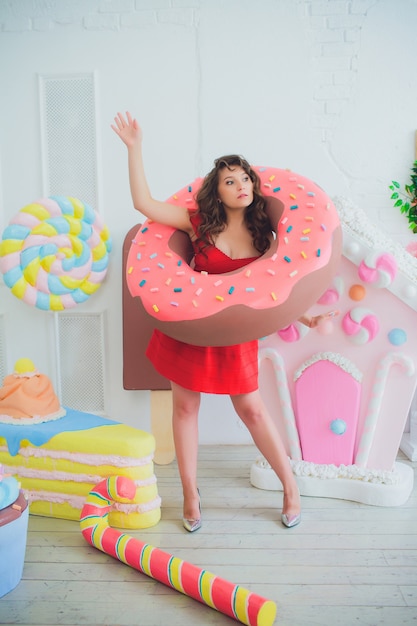 Cute girl posing with pink donuts, fooling around, dessert, bad food, looks into the hole in the donut, keeps donuts by the eyes