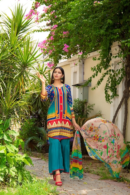 Foto ragazza carina in posa con alberi e piante nel giardino della casa che indossa un abito desi dal design alla moda