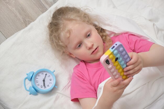 Cute girl preschooler lies with a smartphone in her hands the child plays in the phone games pop it phone case