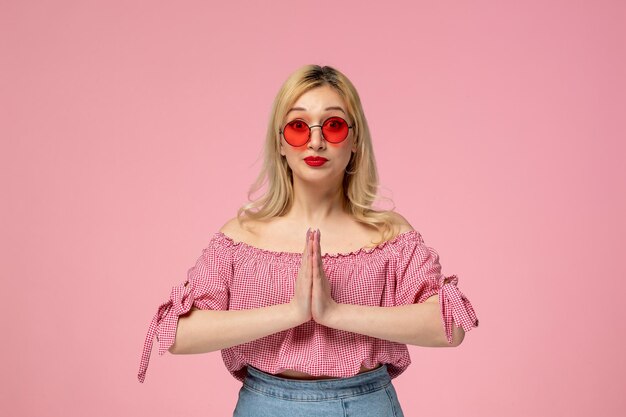 Foto ragazza carina bella signora bionda che indossa occhiali rossi in camicia rosa pregando tenendosi per mano