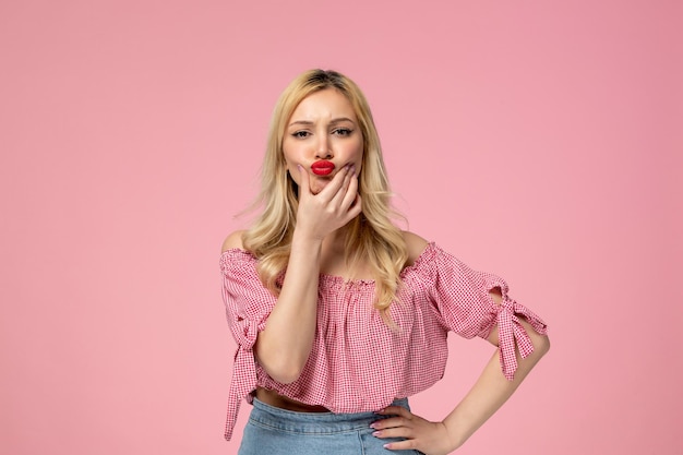 Cute girl pretty blonde lady wearing red lipstick in pink blouse squishing cheeks like a baby