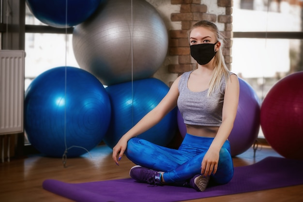 Cute girl in a protective mask sits in a lotus position on the rug. coronavirus (covid-19) protection concept.